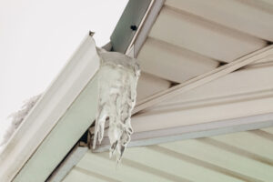 Fragment of roof overhang with icy icicle gutter after thaw.