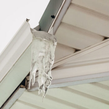 Fragment of roof overhang with icy icicle gutter after thaw.