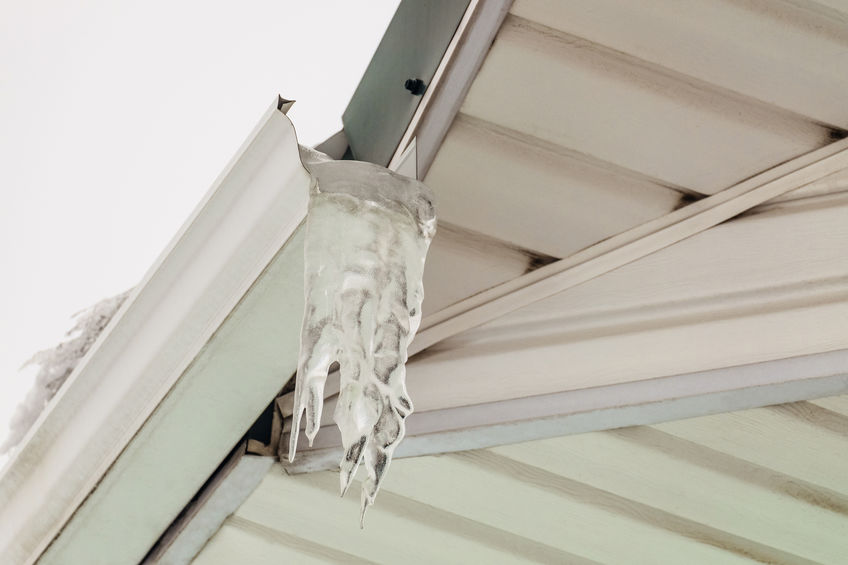 Fragment of roof overhang with icy icicle gutter after thaw.