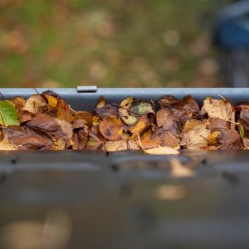 a portrait of a gutter on a roof full of colorful fallen leaves during fall season. cleaning the clogged gutter is an annual chore for many people in order to the rain water flow away properly.